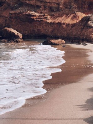 A beach with waves reaching the shore, surrounded by rocky cliffs. - Alfiea Home & Studio (Artemis)