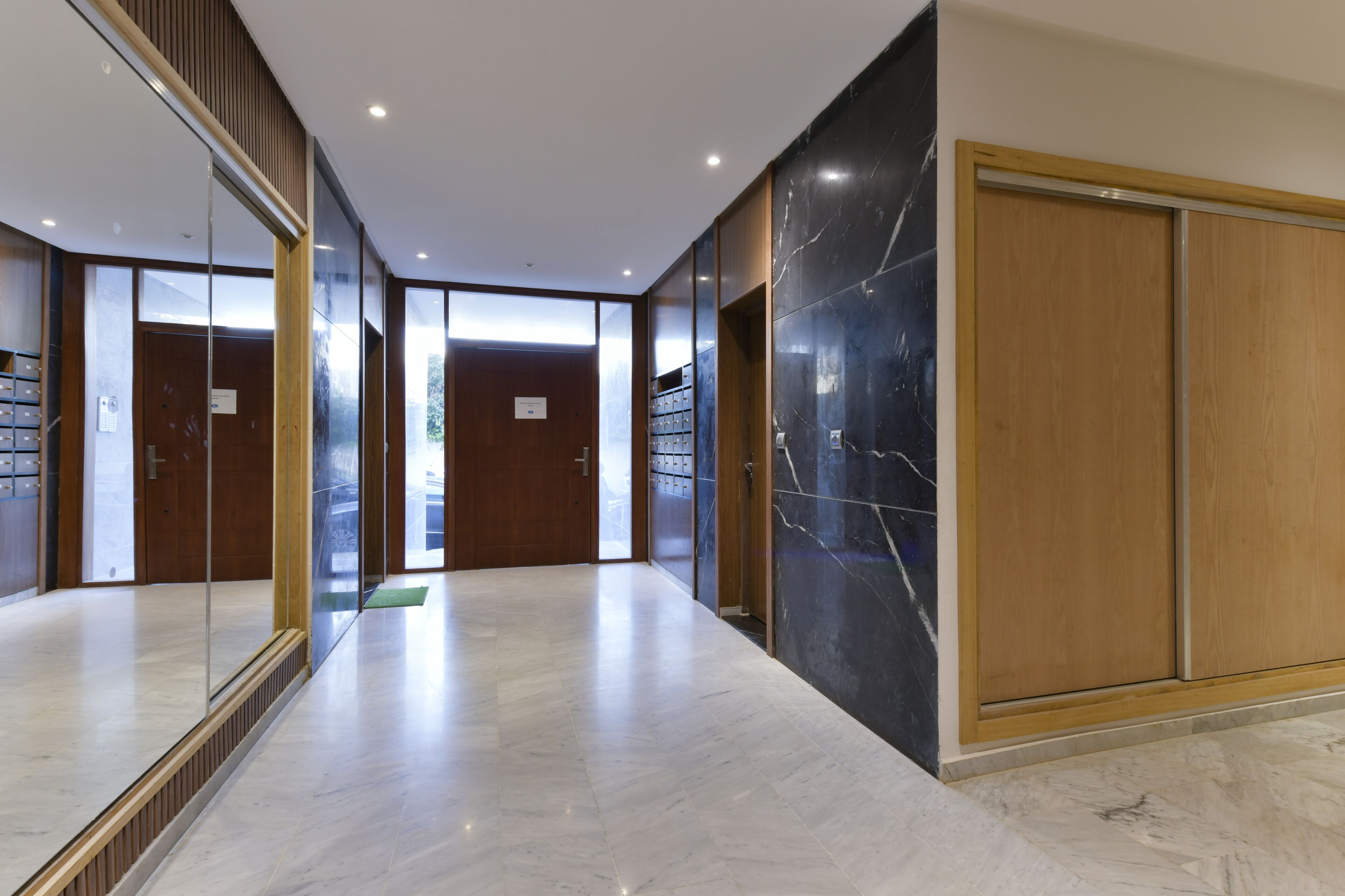 Un couloir moderne avec un sol en marbre, des portes en bois et un grand miroir.