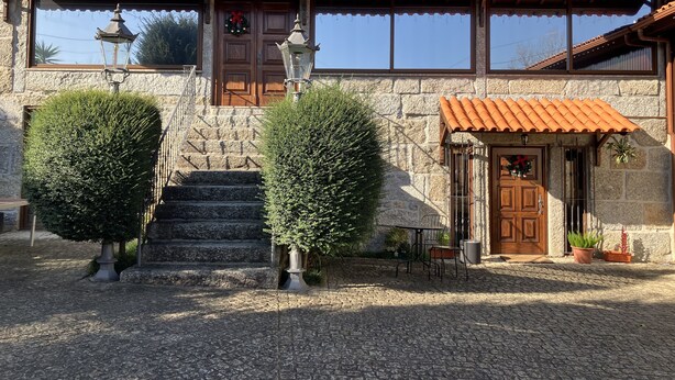 A stone building with a tiled roof, a wooden door, and a small table with chairs outside. - Bergui Guesthouse  (Guimarães)