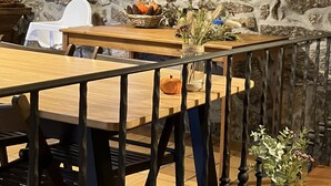 A rustic interior with a stone wall, wooden table, chairs, and a shelf with bottles. - Bergui Guesthouse  (Guimarães)