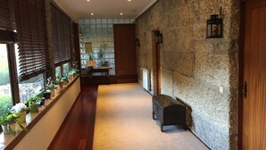 A hallway with a stone wall, wooden flooring, a bench, and potted plants by the windows. - Bergui Guesthouse  (Guimarães)