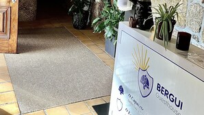 A reception area with a stone wall, a wooden door, and a reception desk labeled "BERGUI". - Bergui Guesthouse  (Guimarães)