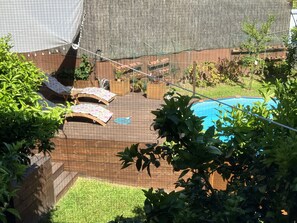A backyard with a wooden deck, a swimming pool, and two sun loungers with umbrellas. - Bergui Guesthouse  (Guimarães)