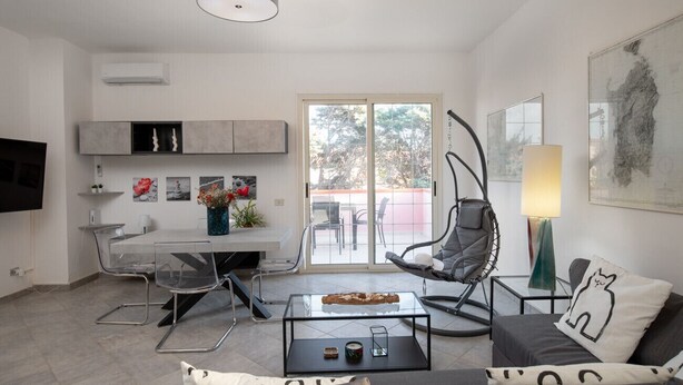 Una sala de estar moderna con una mesa de centro de vidrio, un sofá, una silla y un comedor con mesa y sillas.