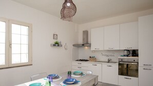 Una cocina moderna con armarios blancos, una estufa a gas, un horno y una lámpara colgante.