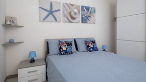 Un dormitorio con cama, dos almohadas, una mesita de noche, una lámpara y decoración en la pared.