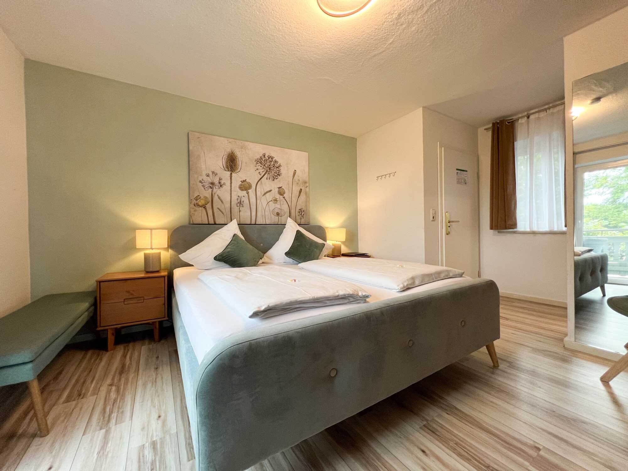 A bedroom with a bed, bedside tables, a nightstand, a chair, a window with curtains, and a door.