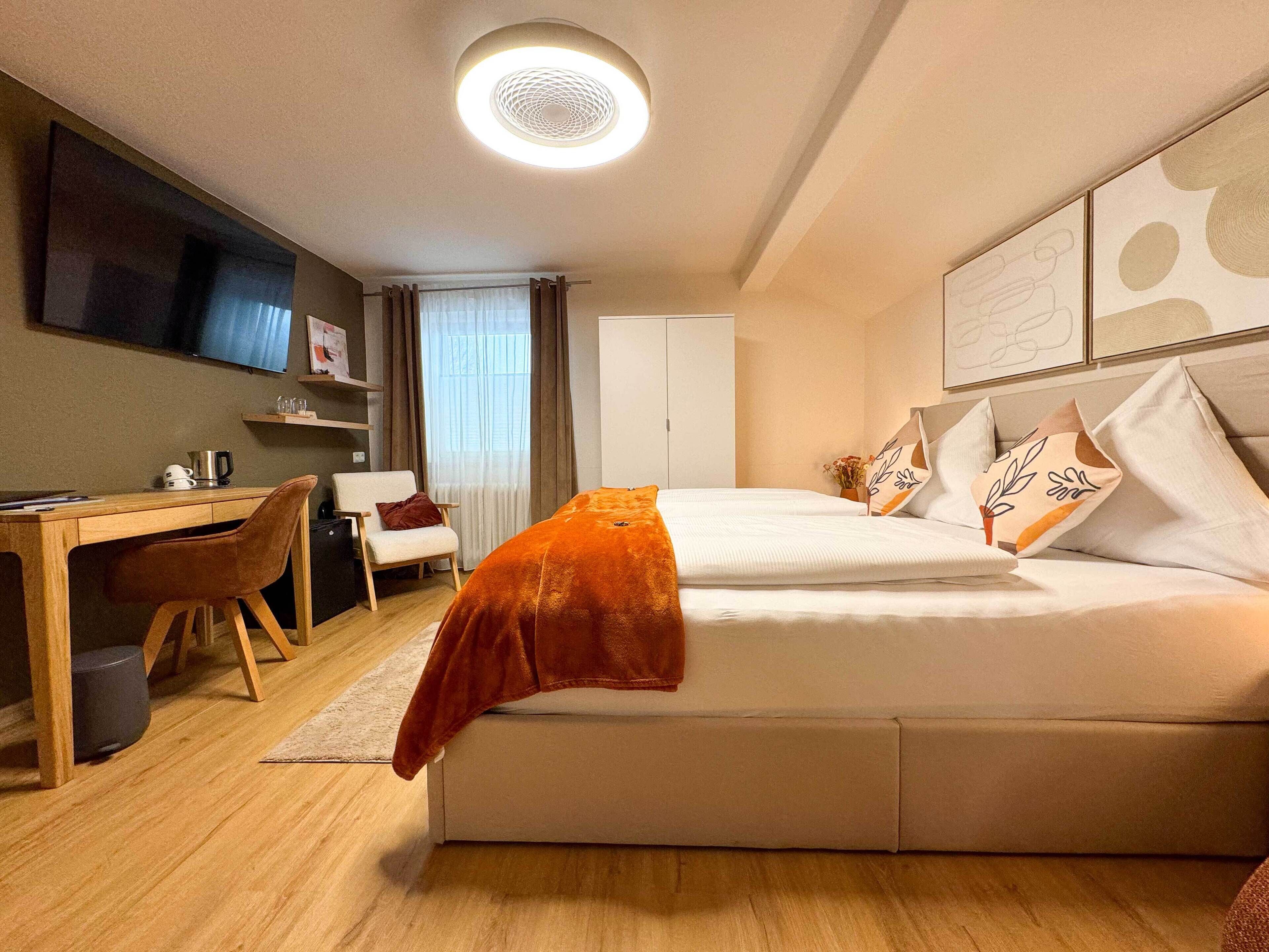 A modern hotel room with a bed, a desk, a chair, and a TV mounted on the wall.