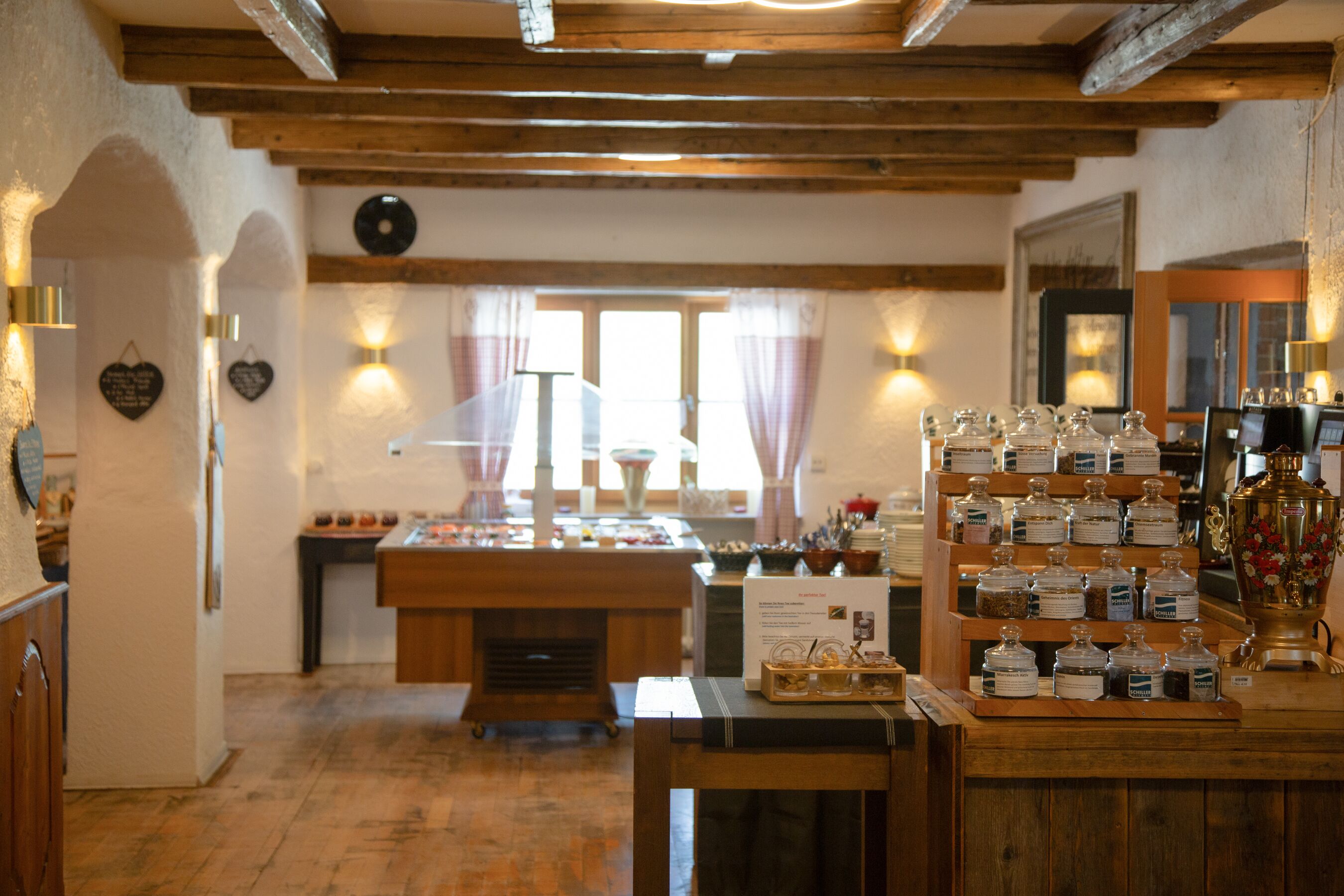 A rustic interior with wooden beams, a buffet table with food items, and a display of jars.
