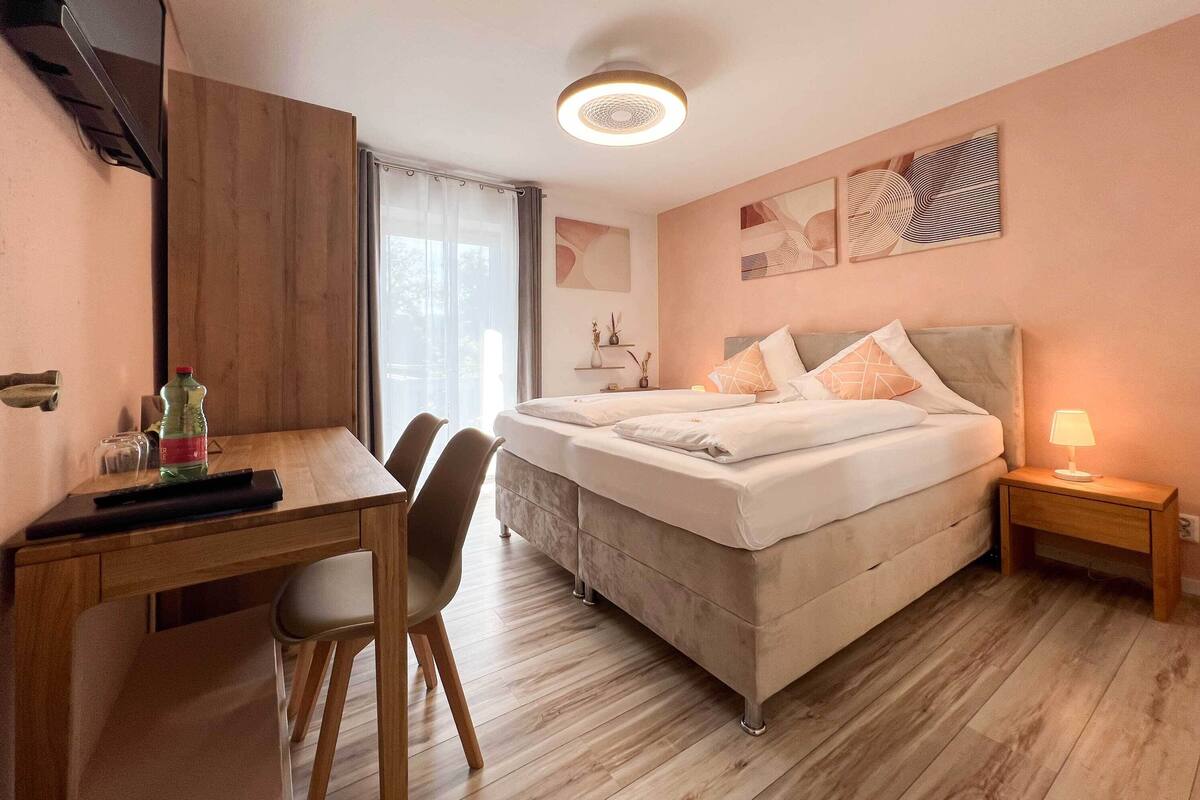 A bedroom with a bed, bedside table, lamp, and a desk with chairs.