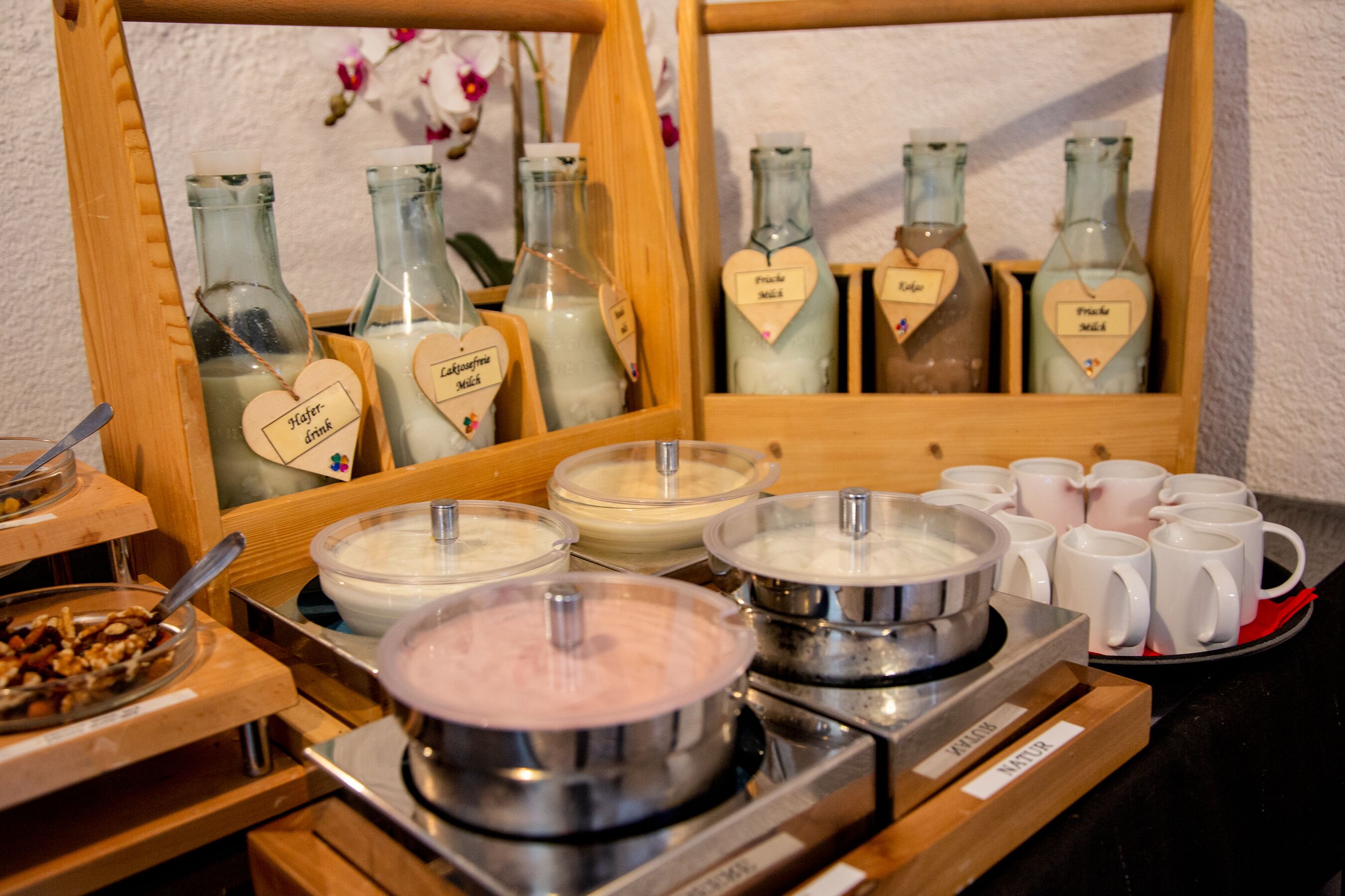 A buffet setup with various food and drink stations, including bowls of soup and milk, and bottles labeled with heart-shaped tags.