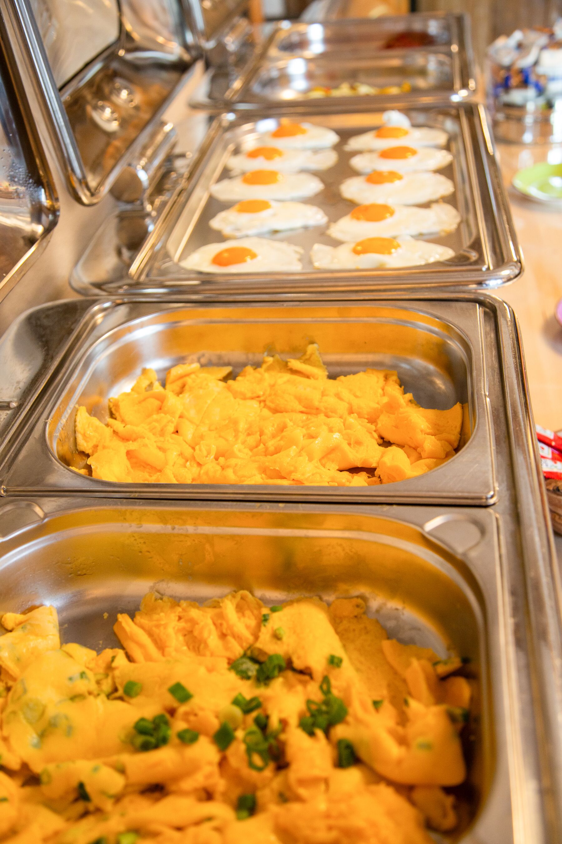 A buffet with various food options including scrambled eggs, macaroni and cheese, and a dish garnished with green onions.