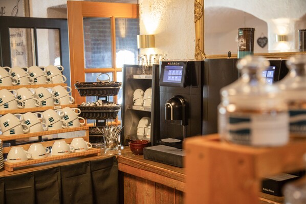 A coffee shop interior with a coffee machine, cups, and a display of mugs. - Gästehaus Sieben Zimmer am See (Prien am Chiemsee)