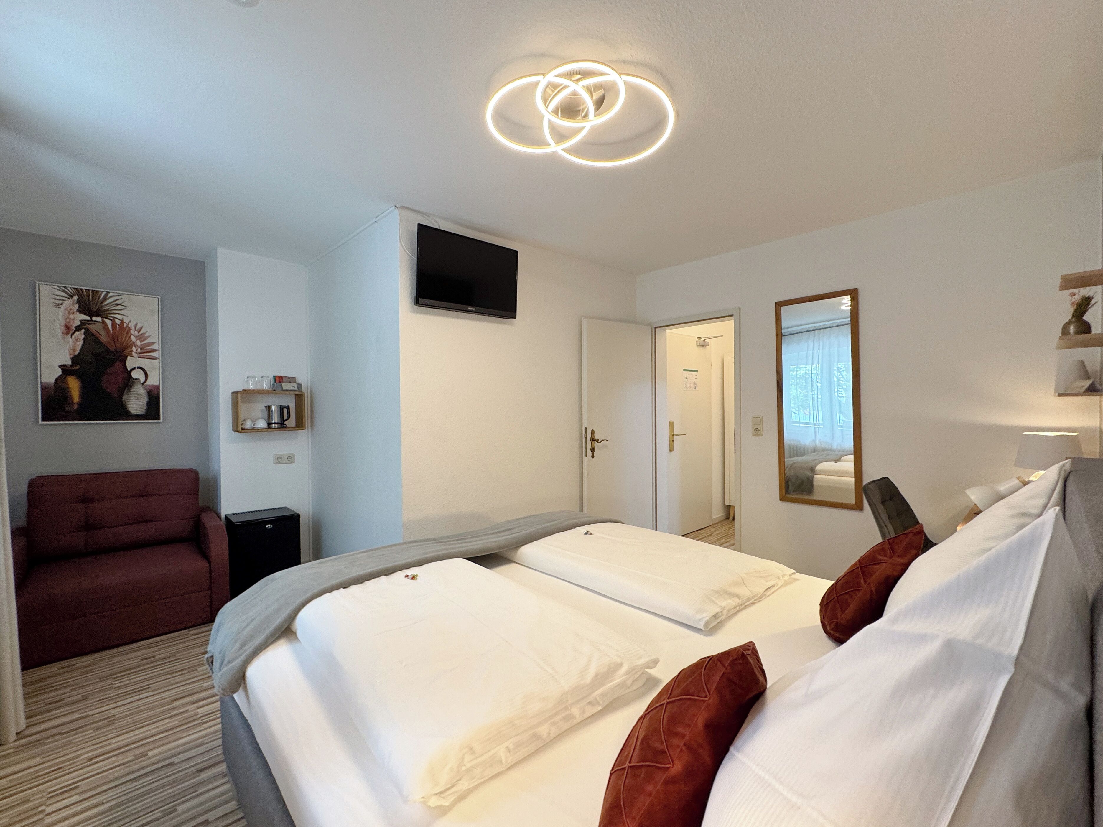 A hotel room with a bed, a red armchair, a TV, and a mirror.