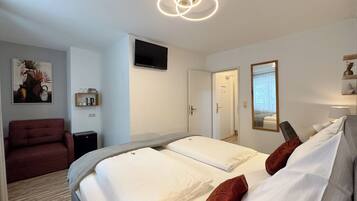 A hotel room with a bed, a red armchair, a TV, and a mirror.