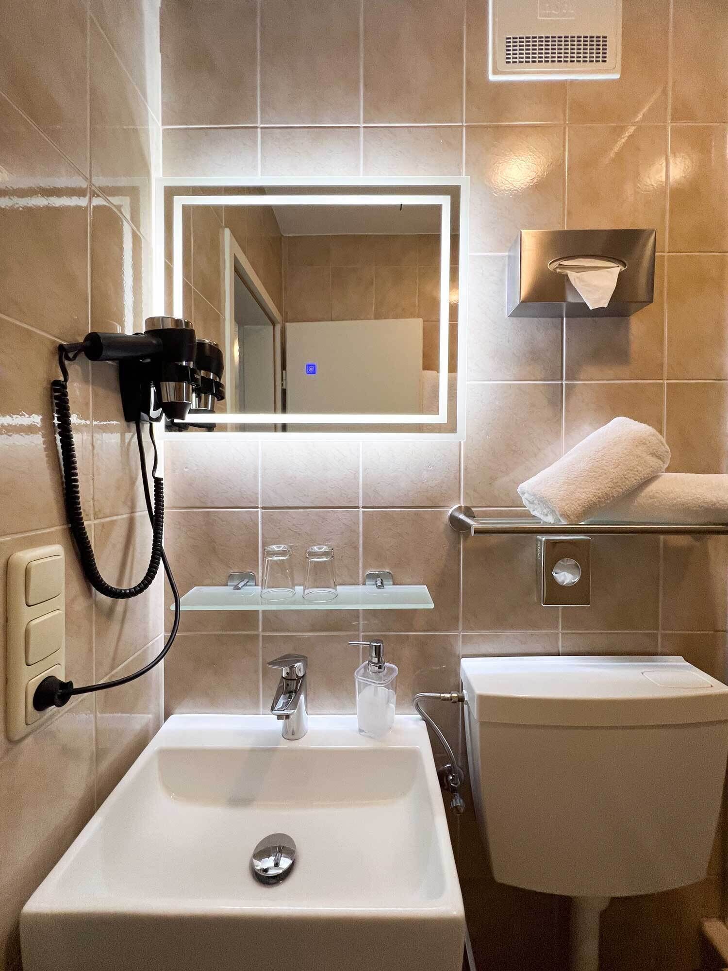A modern bathroom with a large mirror, a sink, a towel rack, and a hairdryer on the wall.