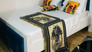 A bed with a white mattress, blue headboard, and colorful pillows. - Lux Suites Bamburi Cozy Apartments (Mombasa)