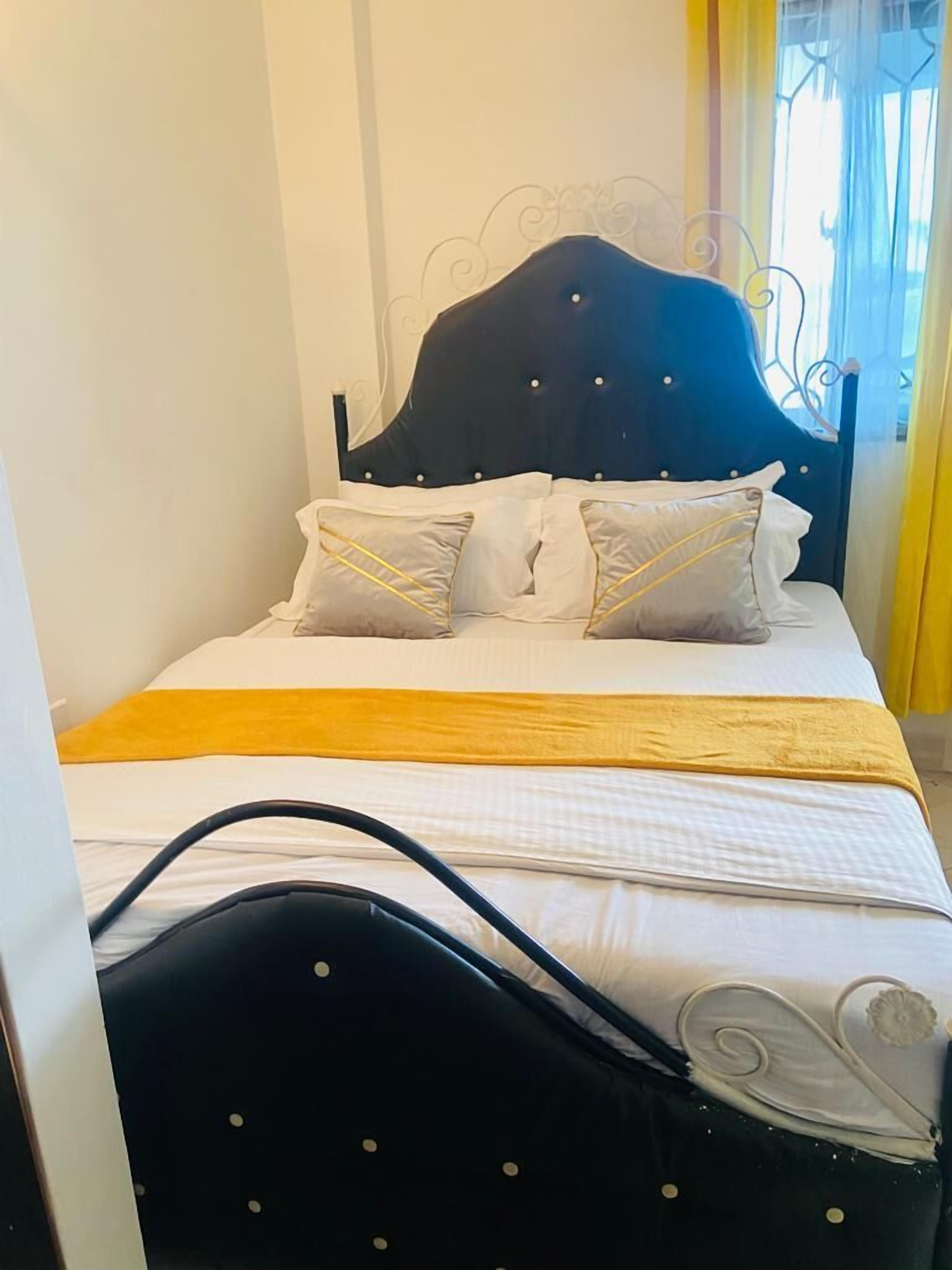 Ein Bett mit dunkelbrauner Kopfteil, weißer Bettwäsche und einem gelben Akzent.