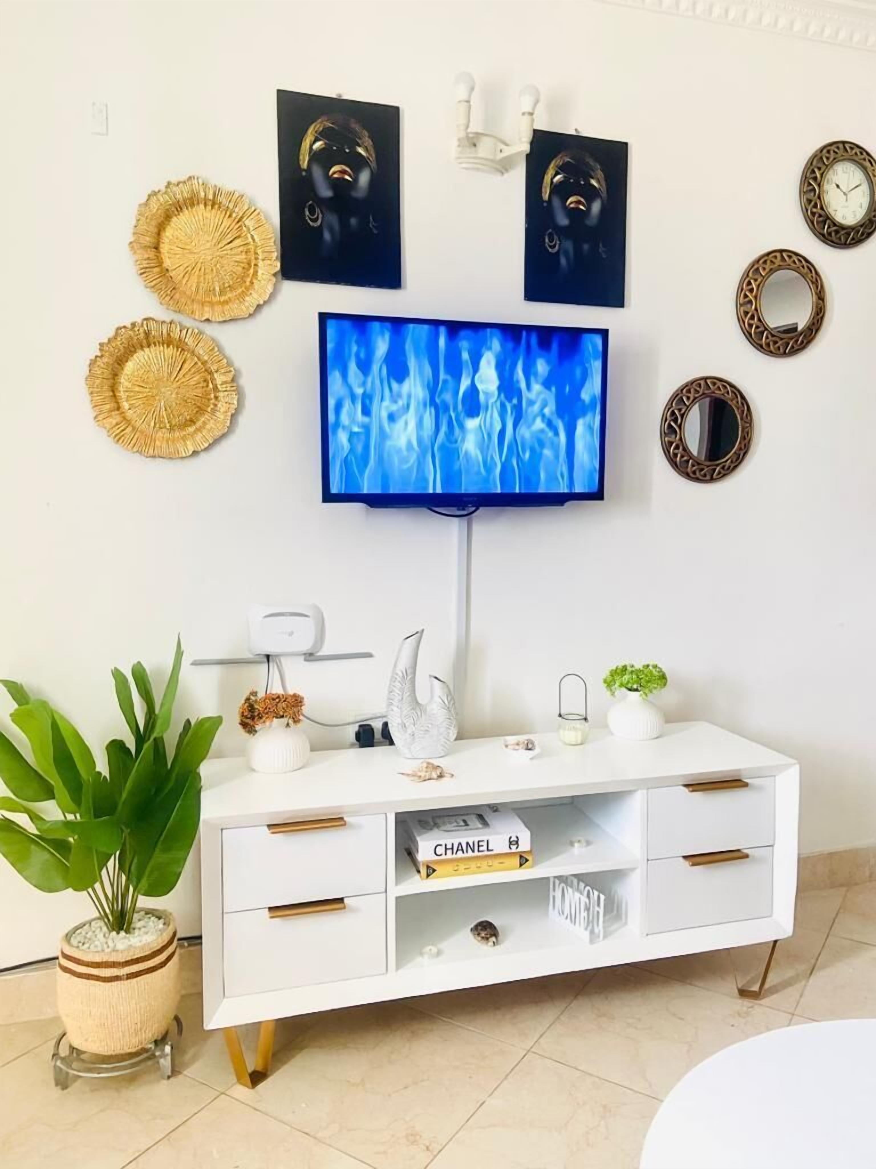 Una sala de estar moderna con un televisor de pantalla plana montado en la pared, rodeada de objetos decorativos y una mesa consola blanca.