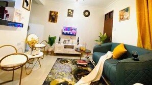 A living room with a sofa, a TV, a ceiling fan, and a dining area with chairs and a table. - Lux Suites Bamburi Cozy Apartments (Mombasa)