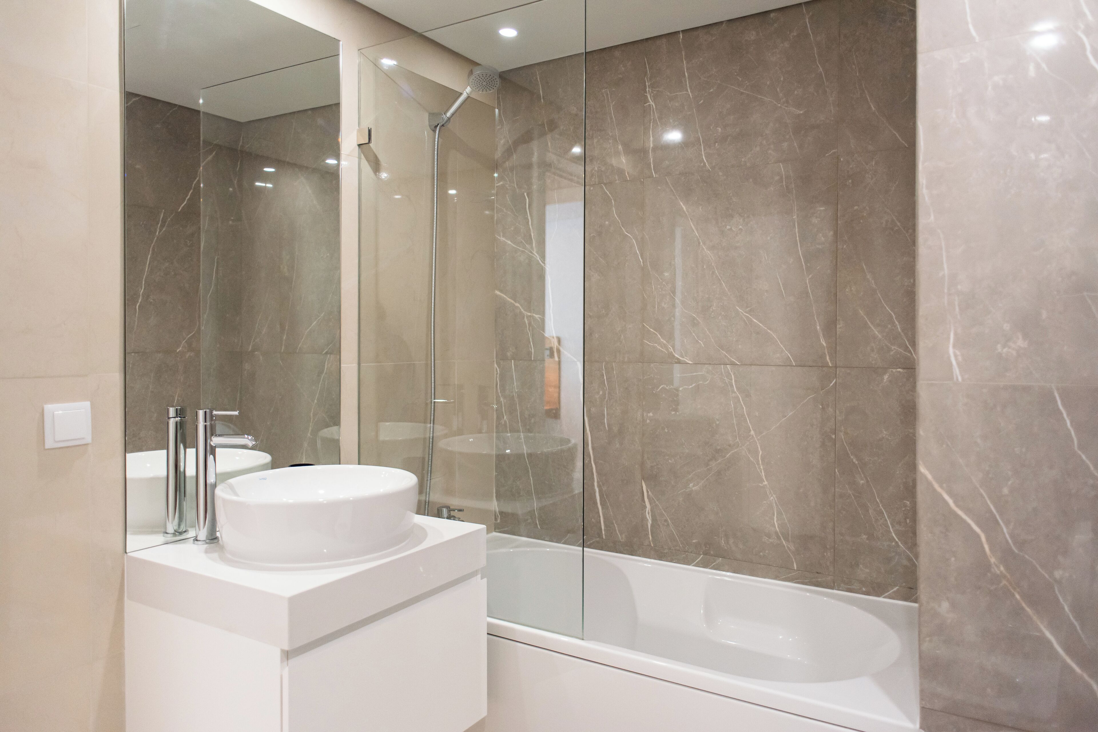 Une salle de bain moderne avec un lavabo blanc, une douche à parois de verre et des murs en marbre.