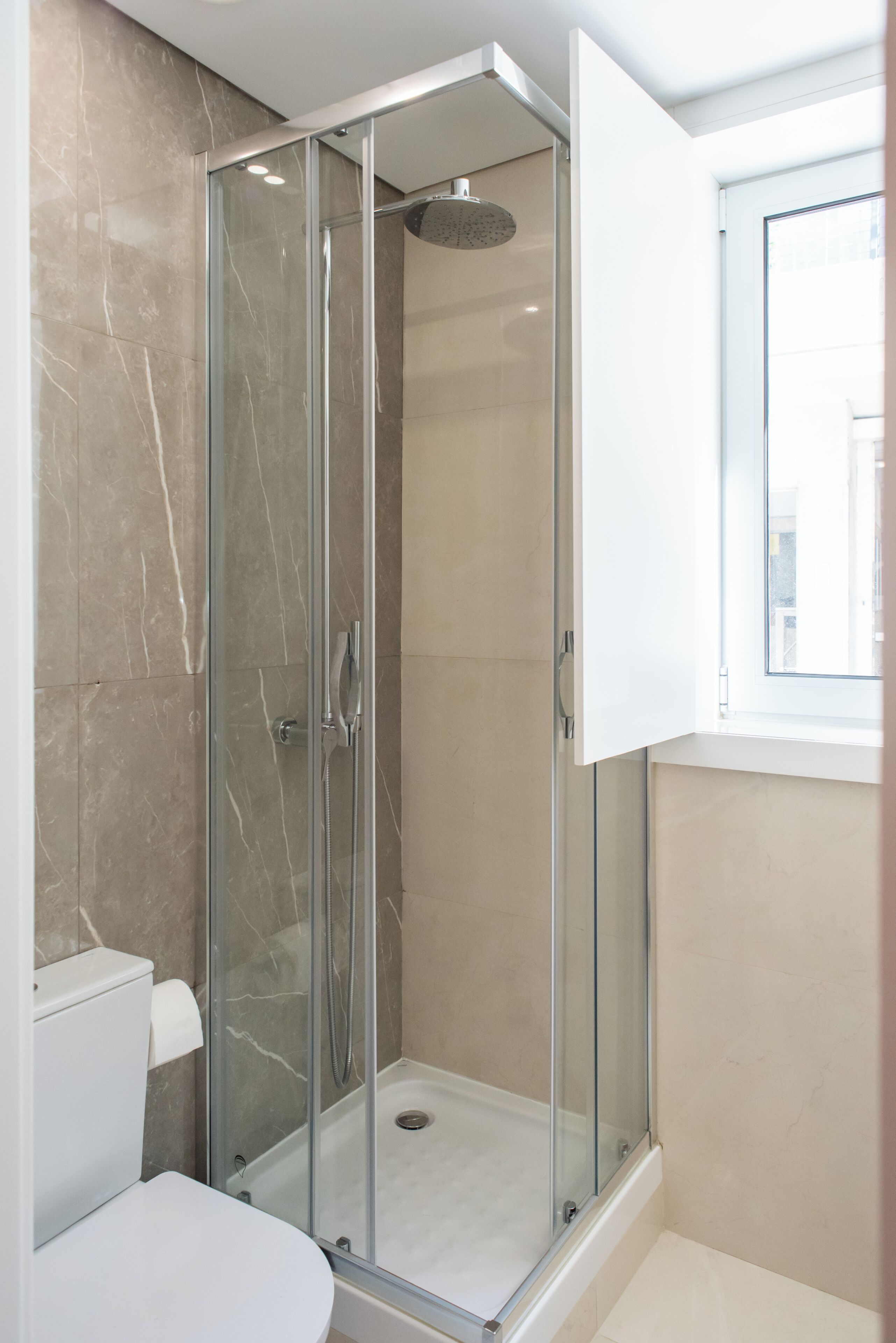 Un baño moderno con ducha envuelta en vidrio, inodoro y ventana.