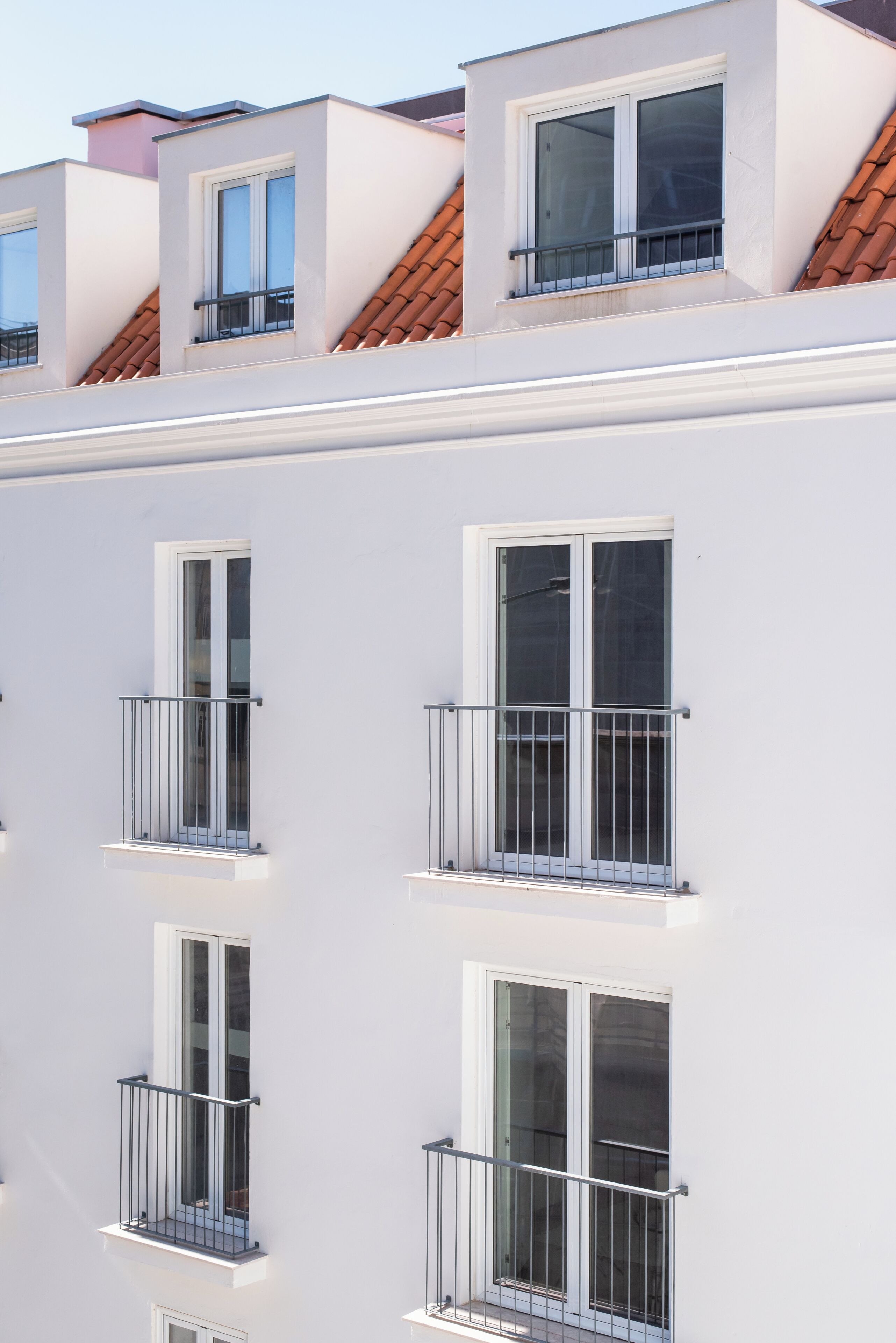 Un edificio de varios pisos con paredes exteriores blancas, múltiples balcones con barandillas de metal y ventanas amplias.