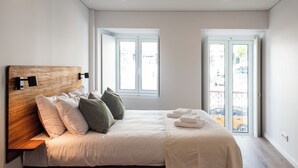 Een moderne slaapkamer met een houten hoofdbord, een groot bed met witte lakens, twee ramen en uitzicht op buiten.