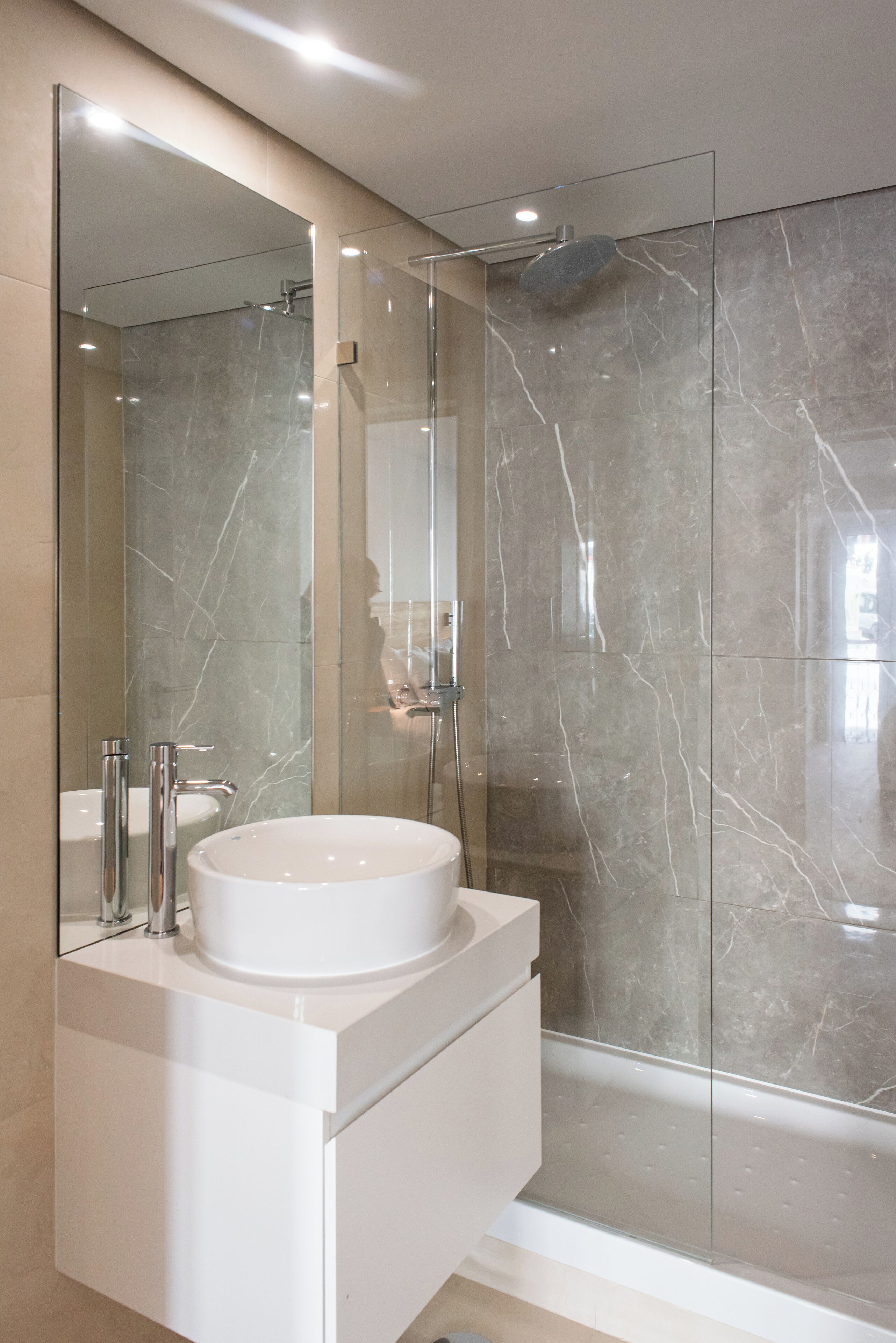 Een moderne badkamer met een douchecabine van glas, een witte wastafel en een grote spiegel.