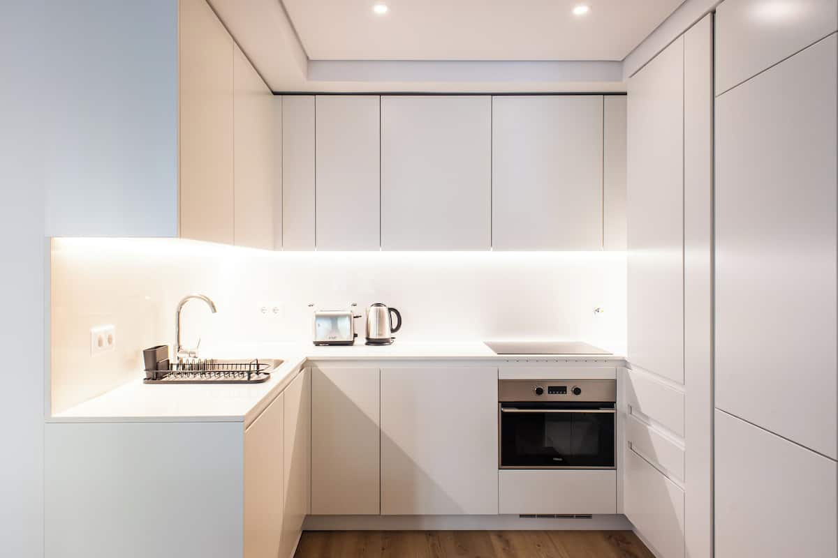 Una cocina moderna con armarios blancos, horno empotrado, microondas y hervidor sobre la encimera.