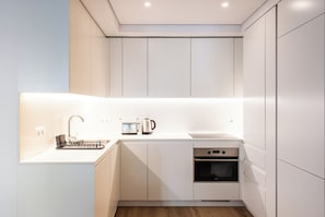 A modern kitchen with white cabinetry, a built-in oven, a microwave, and a kettle on the countertop.
