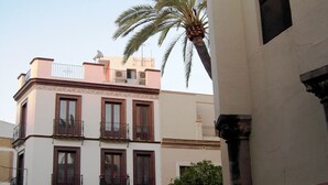 Un edificio de varios pisos con balcones, un coche estacionado y una palmera.