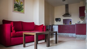 Una sala de estar con un sofá rojo, una mesa de centro de madera y una cocina al fondo.