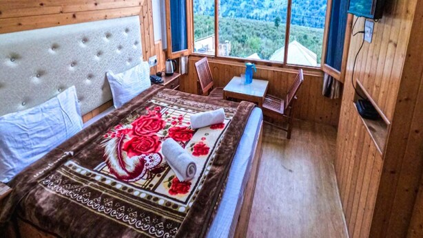 Ein Schlafzimmer mit einem großen Bett, einem Holzkopfteil, einem Fenster mit Blick auf Bäume, einem kleinen Tisch und einem an der Wand befestigten Fernseher.