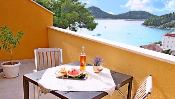 A balcony with a table set for two, featuring a bottle, glasses, and a watermelon slice.