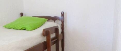 Een enkel bed met houten frame, een groen kussen en een klein nachtkastje met een witte lamp en een groene vaas.