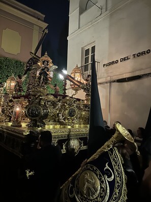 Un carro allegorico riccamente decorato con figure religiose e disegni elaborati, che passa davanti a un edificio con la scritta "PEDRO DEL TORO".