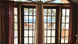 A room with a large window overlooking a beach, featuring a view of palm trees and the sea. - Beautiful 5 bedroom beachfront villa with private pool just 2.5 miles from town (San Pedro)