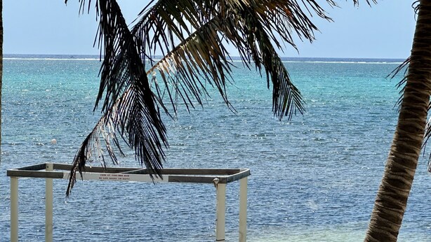 A wooden deck with two wooden chairs and a table, overlooking a clear blue sea. - Beautiful 5 bedroom beachfront villa with private pool just 2.5 miles from town (San Pedro)