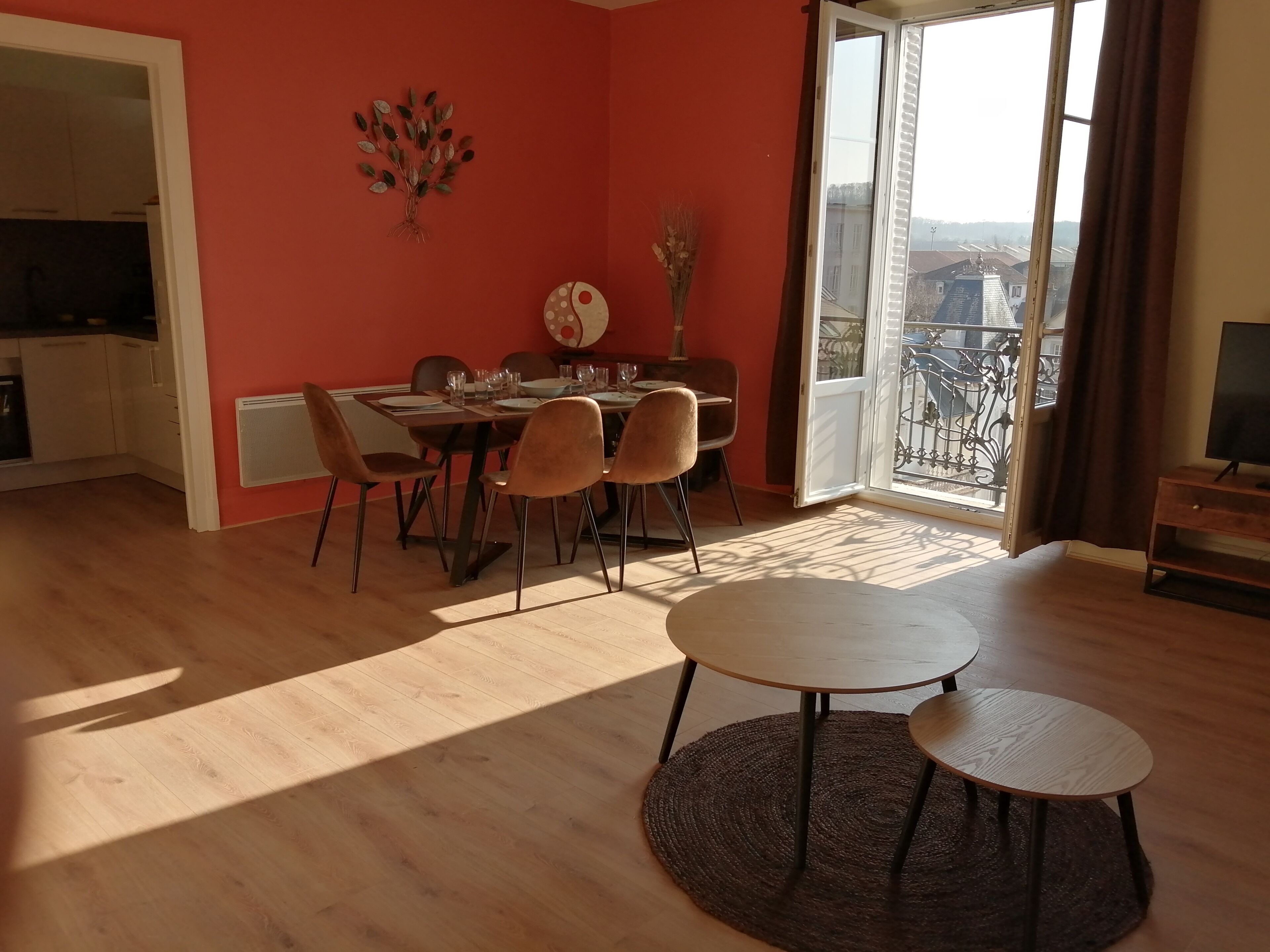 A dining area with a table set for four, a decorative wall piece, and a view through a sliding door.