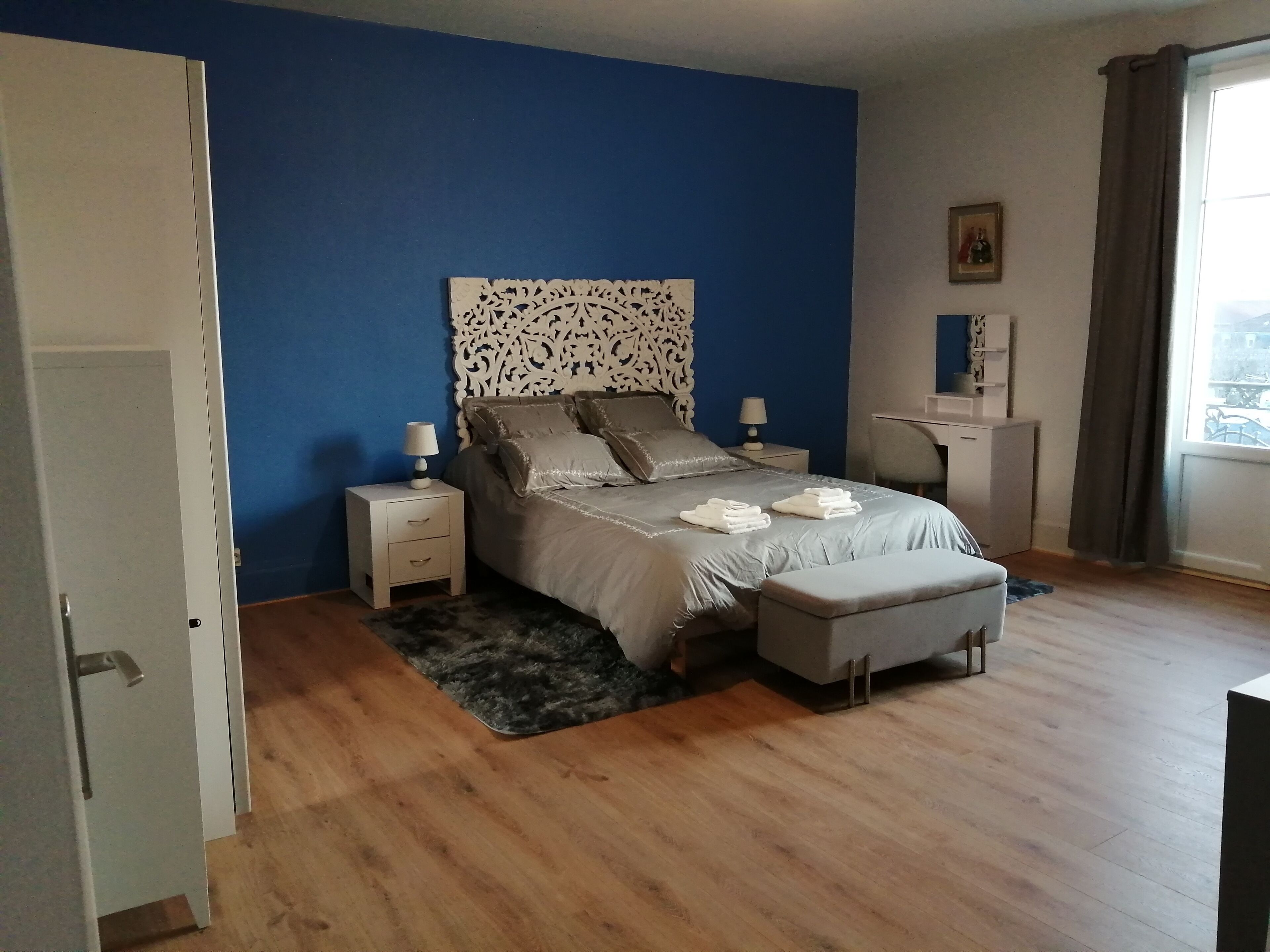Un dormitorio con cama, mesitas de noche, un escritorio y una ventana con cortinas.