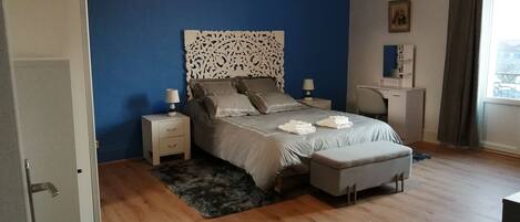Un dormitorio con cama, mesitas de noche, un escritorio y una ventana con cortinas.