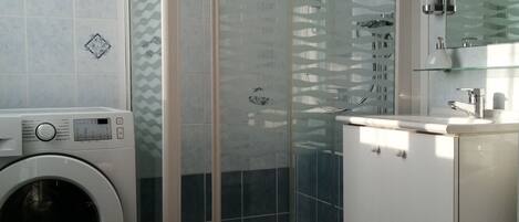 A compact bathroom with a glass-enclosed shower, a washing machine, and a toilet.
