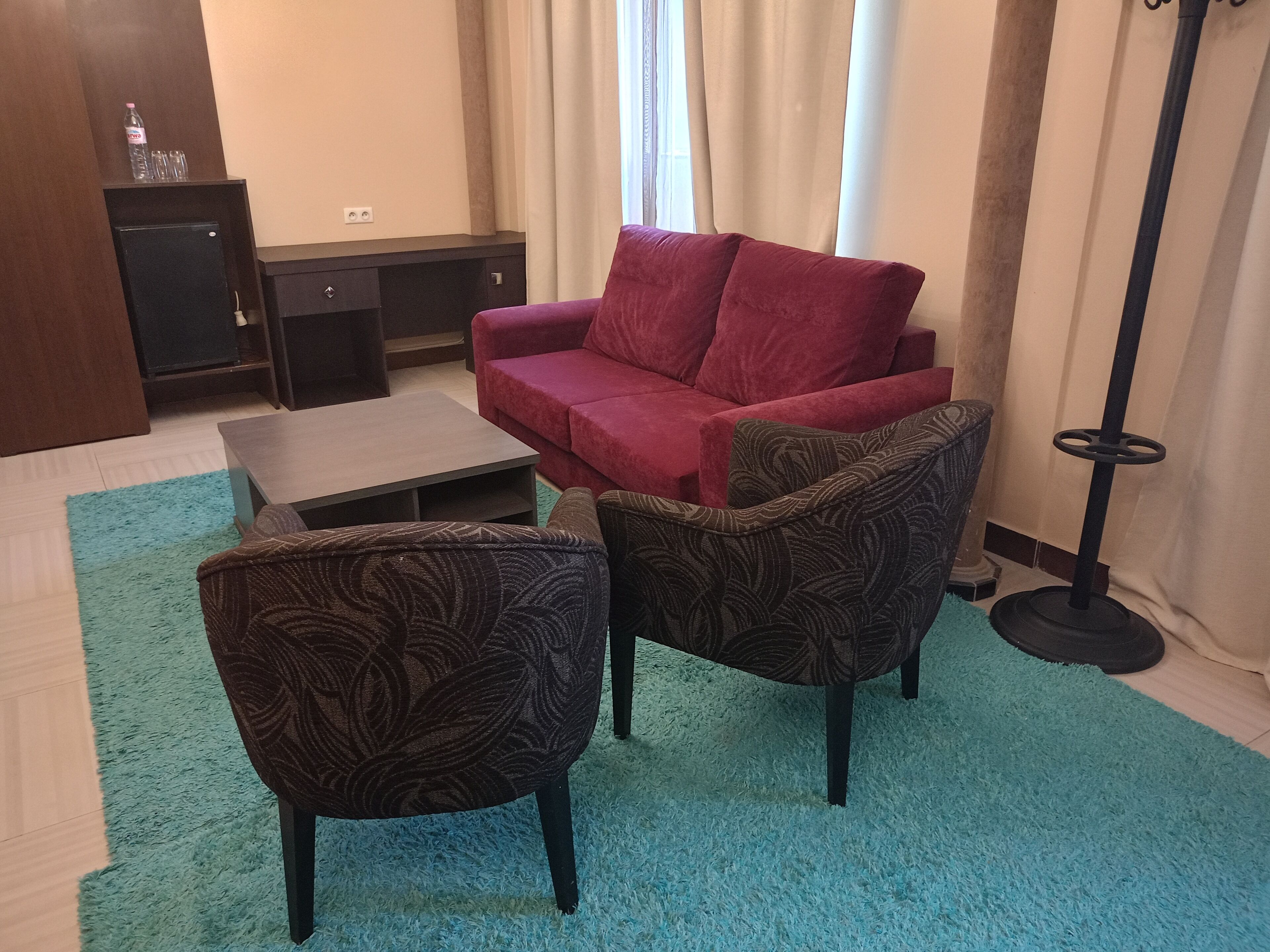 Una sala de estar con un sofá rojo, dos sillones estampados, una mesita de centro y un televisor pequeño sobre un mueble.