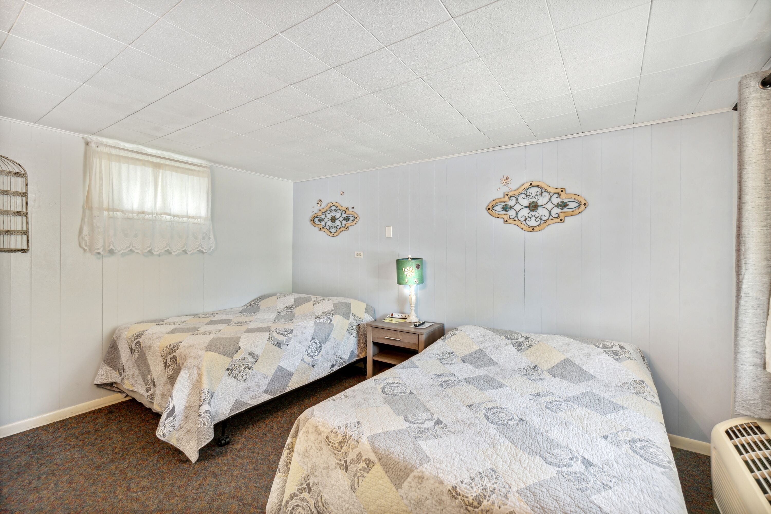 Une chambre avec deux lits, une fenêtre avec un rideau, une lampe fixée au mur et un radiateur.