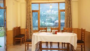 Comedor con una mesa dispuesta para cuatro personas, sillas de madera y ventanas amplias con cortinas.