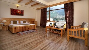 Una habitación amplia con una cama de madera, un sofá y una silla, un ventanal con cortinas y un cuadro en la pared.