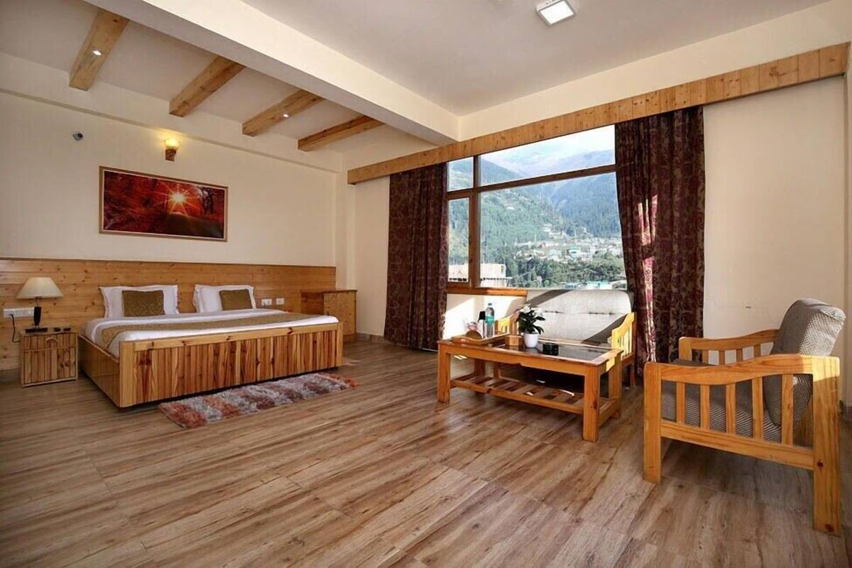 A spacious room with a wooden bed, a sofa, and a chair, a large window with curtains, and a painting on the wall.