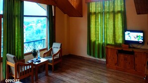 Una habitación acogedora con vigas de madera, una mesa de comedor con sillas, un televisor y ventanas grandes con cortinas verdes.