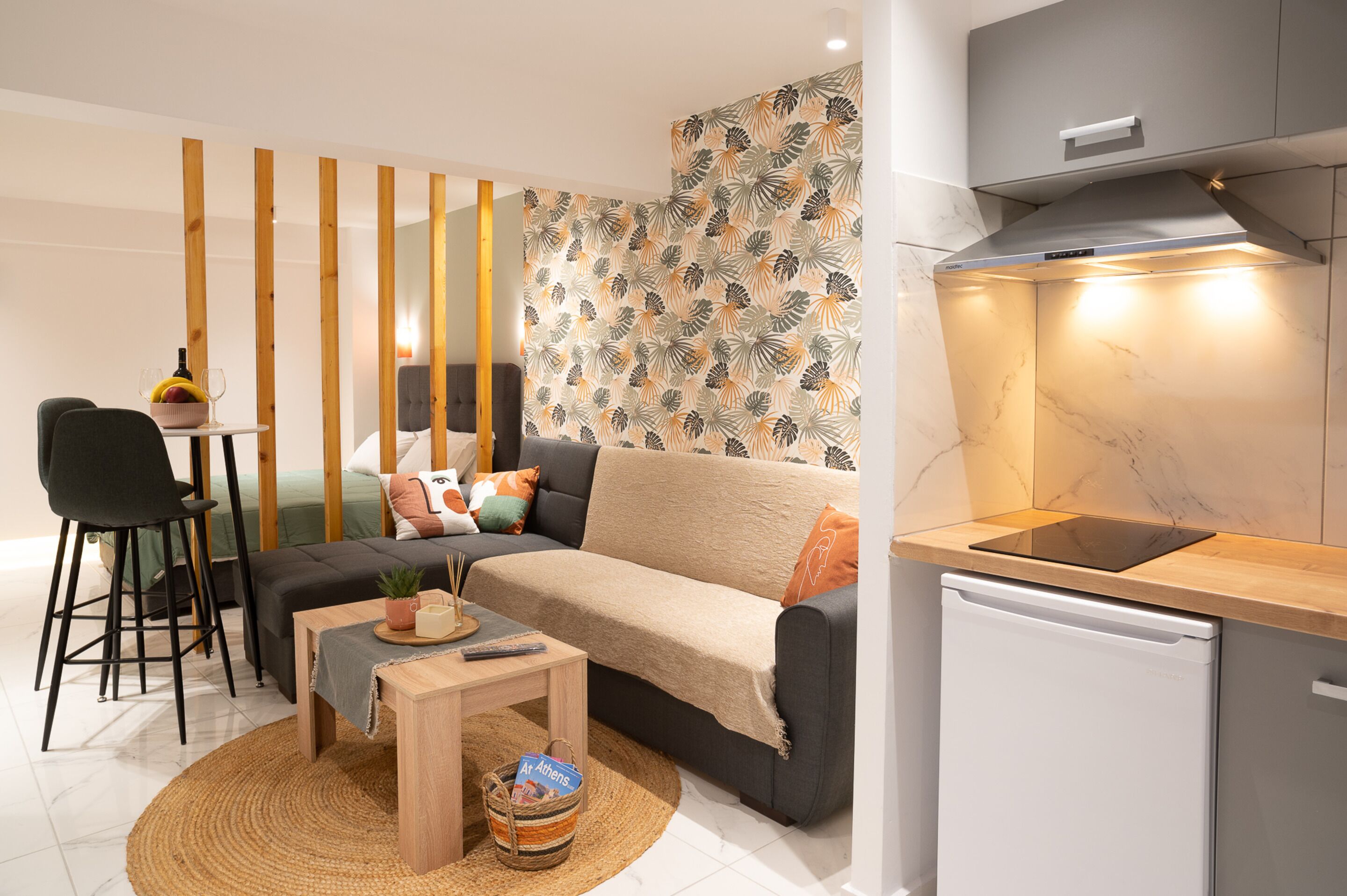 A modern living room with a sofa, coffee table, and a small kitchen area with a dishwasher.